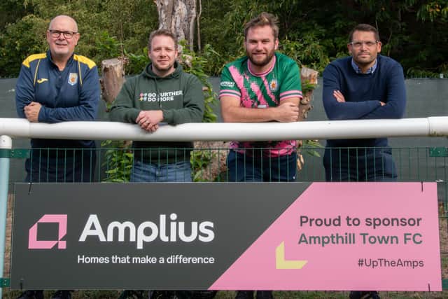 Representatives of Amplius and Ampthill Town Football Club post in front of the new Amplius sponsorship board at the club's home stadium.