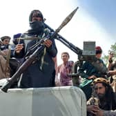 Taliban fighters sit over a vehicle on a street in Laghman province
