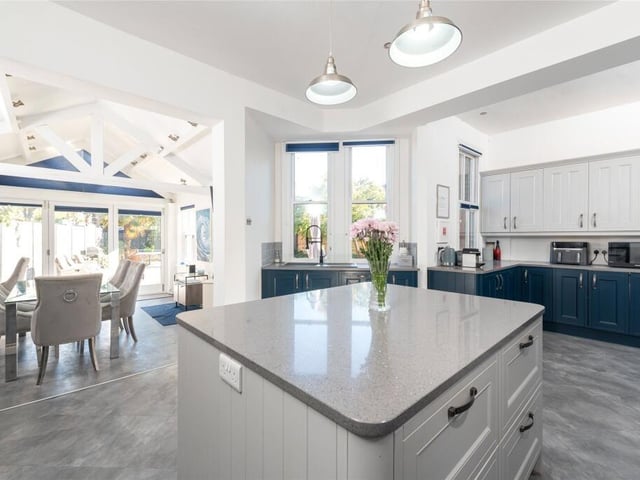 An impressive space, the kitchen has a comprehensive range of custom-built cabinets and a central island, all with granite worksurfaces. A wide aperture with steps leads down to the dining room which has a high ceiling with exposed beams and bi-fold doors to the garden