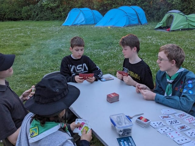 Scouts play cards in a camp while the sun sets