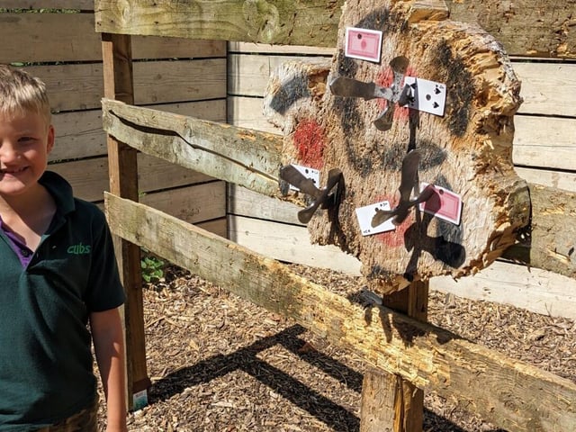 A Cub Scout stands in front of a tomahawk throwing target