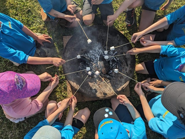 Beaver Scouts sit around a fire pit toasting marshmallows on embers