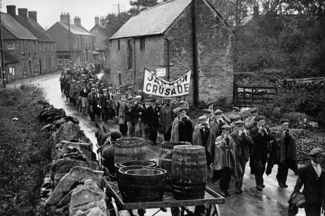 Jarrow marchers passing throught the village of Lavendon, near Bedford, on their way to London, many playing mouth organs to keep spirits up. The Jarrow March was a hunger march during the Great Depression, starting in Jarrow it reached London a month later to put pressure on the coalition government.