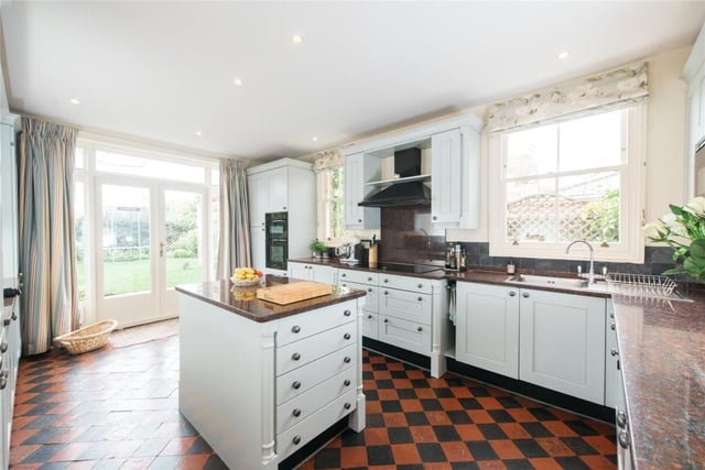 The kitchen is fitted with a range of hand-painted Shaker style units, including a central island, with granite work surfaces and slate tiled splashbacks. Integrated appliances include a five burner gas hob. There are French doors to the garden and black and red quarry tiled flooring
