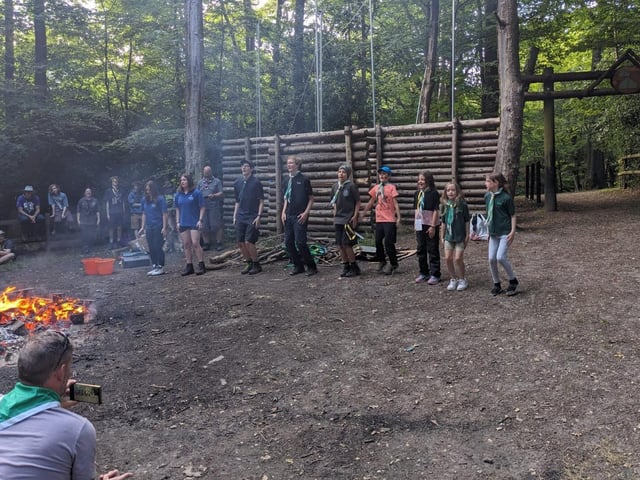 Scouts stand in front of a campfire singning