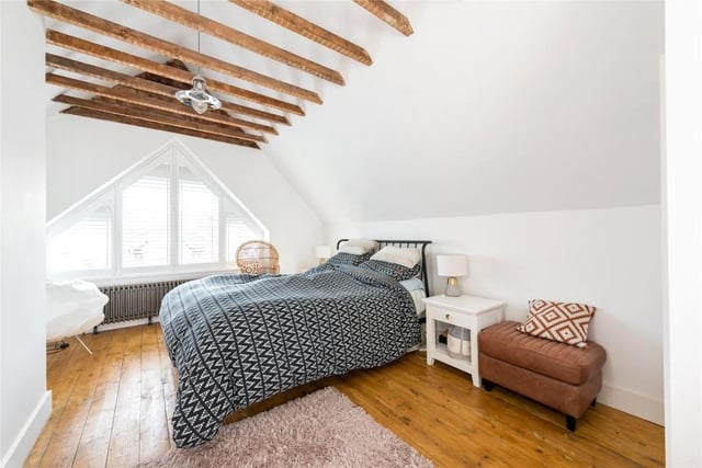 The master bedroom on the second floor has a vaulted ceiling with exposed timbers and brick walls. There is an en suite shower room and access to eaves storage