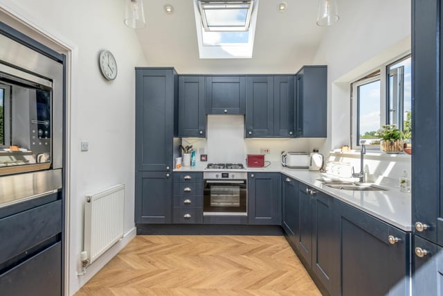 The kitchen features herringbone-effect flooring, trendy navy blue units and glittering quartz work surfaces