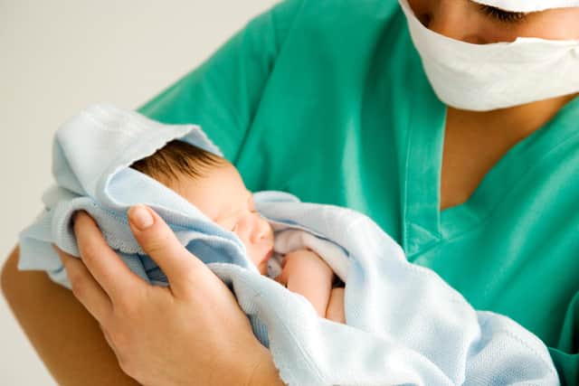 Maternity nurse wearing scrubs holding newborn baby wrapped in blanket