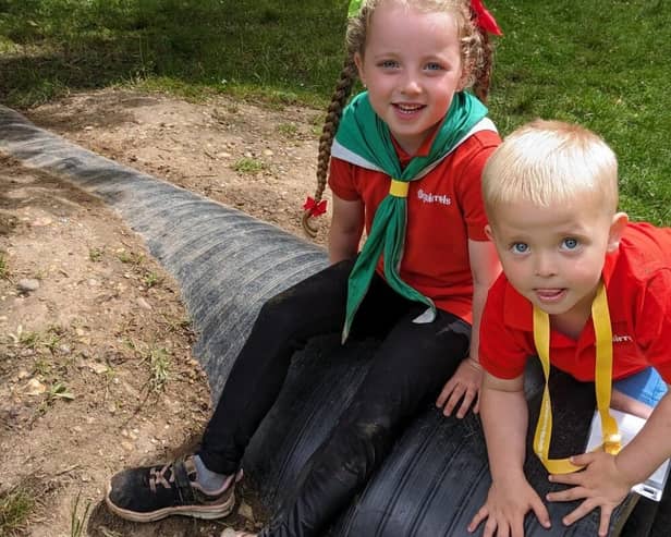 Two Squirrel Scouts sit on a plastic tunnel