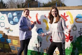 Two young artists proudly stand in front of a cheerful mural on an outdoor wall