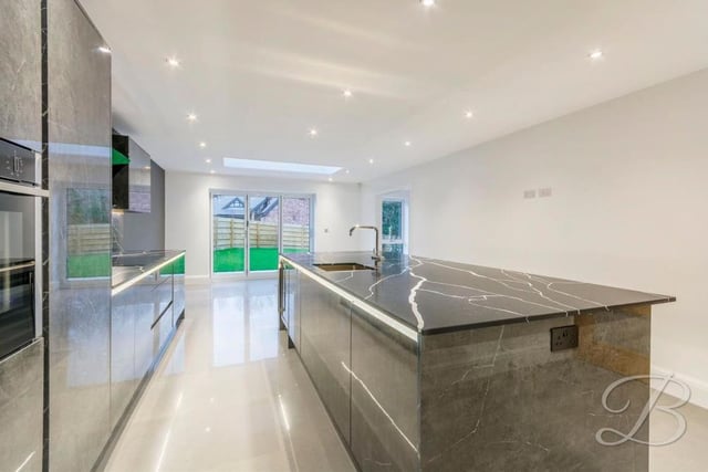 Another view of the high-quality, bespoke kitchen. It features luxurious, branded appliances and slick work-surfaces. At the far end, doors lead out on to the garden at the back.