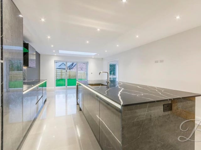 Another view of the high-quality, bespoke kitchen. It features luxurious, branded appliances and slick work-surfaces. At the far end, doors lead out on to the garden at the back.
