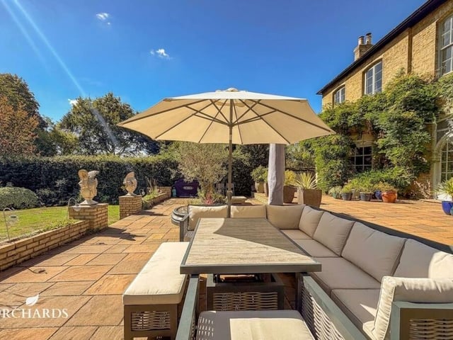 The south-facing grounds extend to approximately 0.89 acres, with broad lawns, established planting and a series of terraces positioned for outdoor dining and entertaining